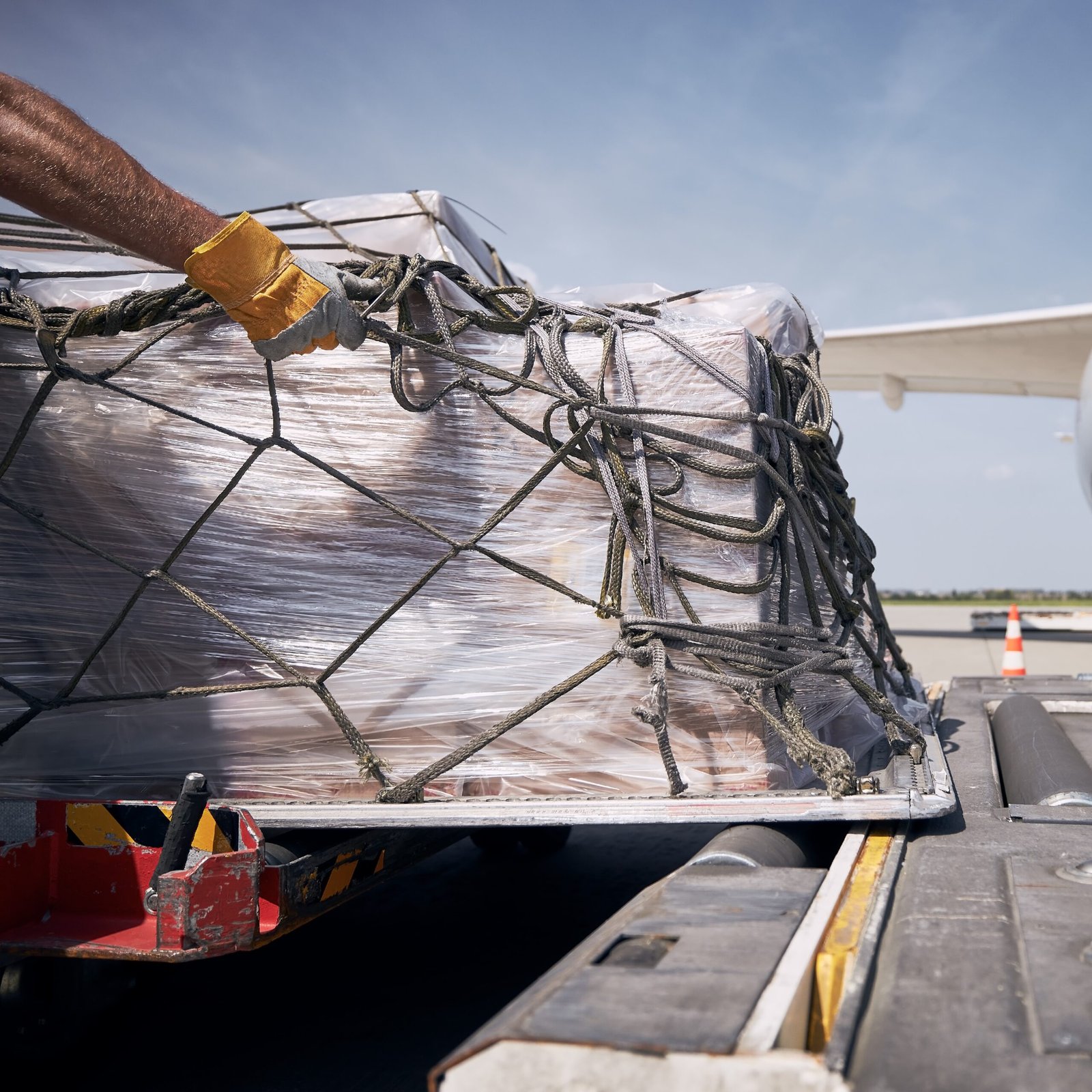 Hand of ground crew during unloading freight airplane. Cargo containers against jet engine of plane.